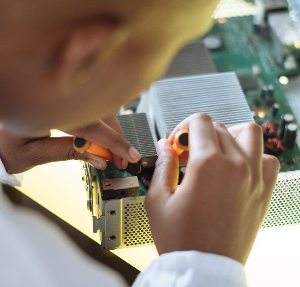 Crop of ethnic system administrator in uniform using screwdrivers and checking motherboard on electronic equipment during work in repair department